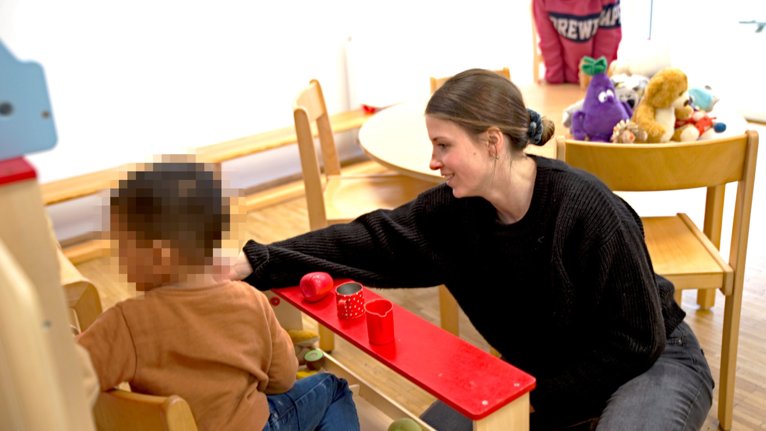 Helles Spielzimmer. Spielende Kinder mit Betreuerin.