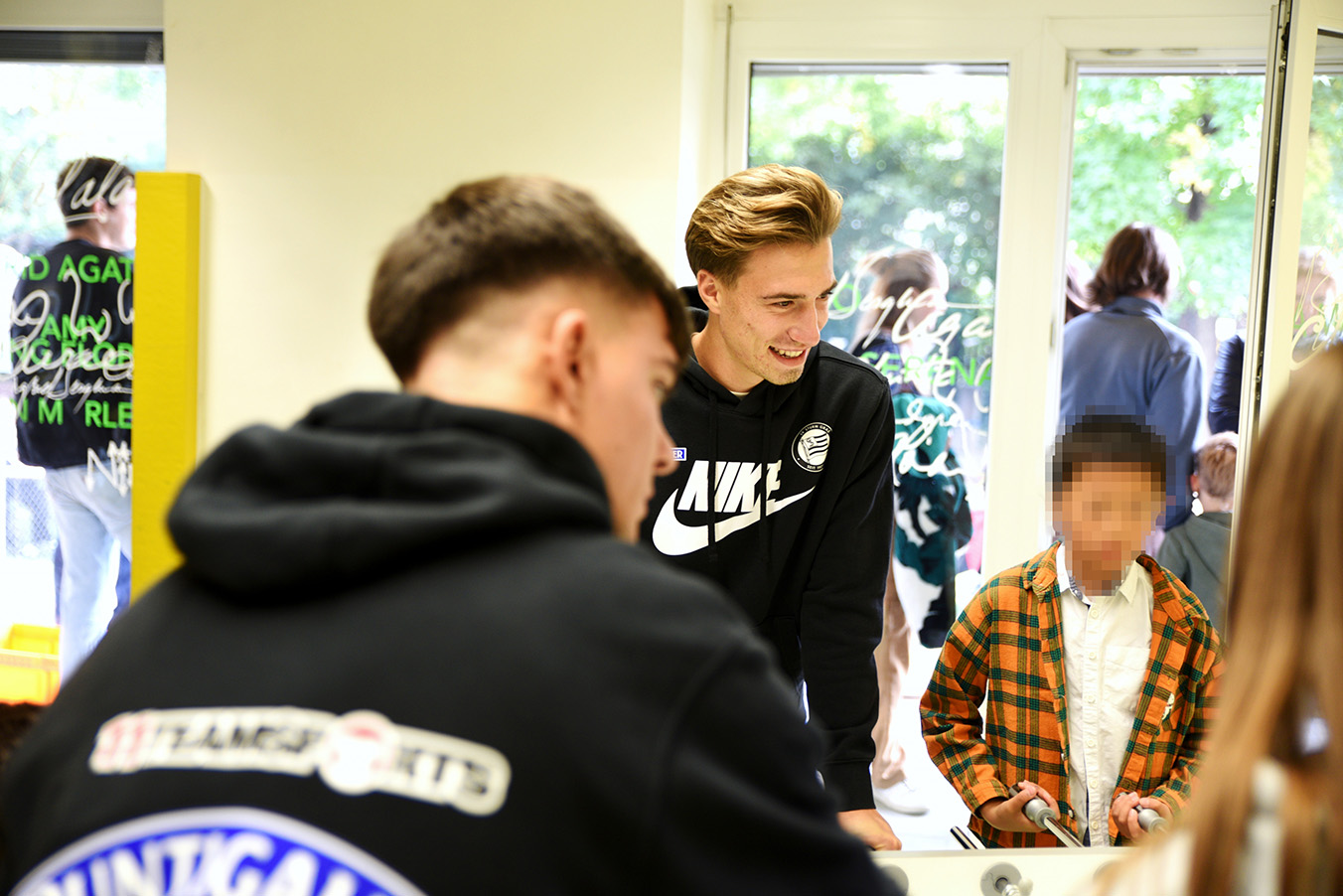 Spieler und Spielerinnen vom SK Sturm spielen Tischfußball mit den Kindern im Frauenhaus Graz.